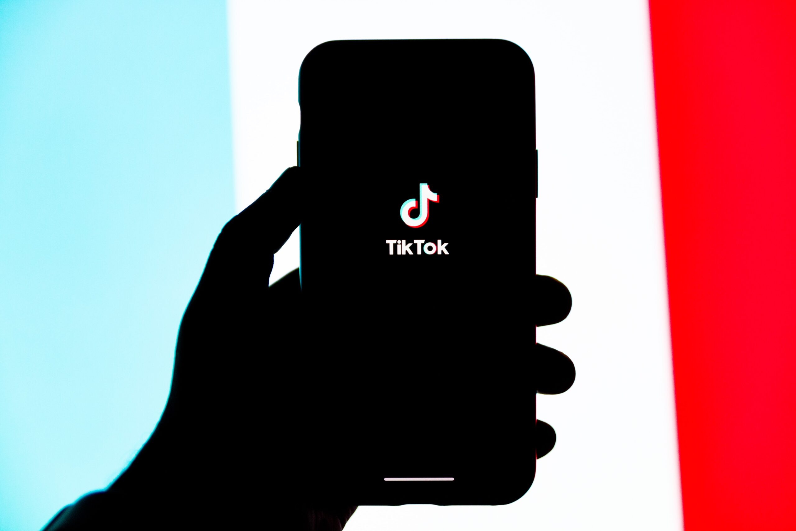 Hand holding cellphone with TikTok logo on screen.