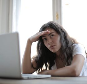 Woman rolling her eyes upward with her hand on her head with a computer in front of her.