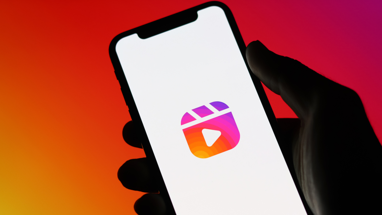 Rainbow background with hand holding a cellphone with Instagram reels logo on it.