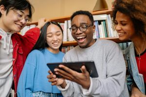 Four people excitedly huddled around an iPad in front of a bookcase.