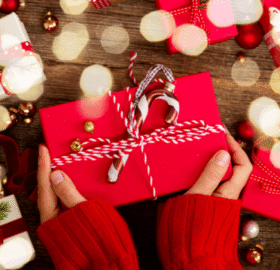 person holding a gift wrapped in red paper with a candy cane ornament