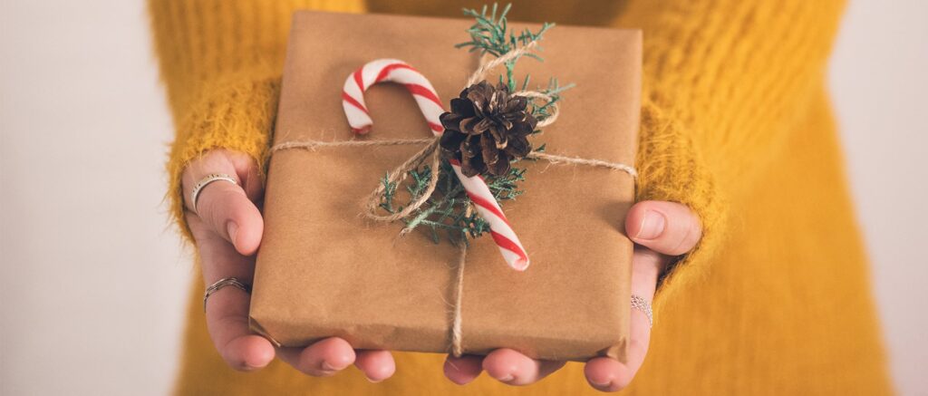 person holding a present wrapped in brown paper with a candy cane and pine cone in the middle of the gift